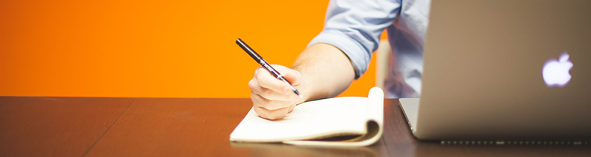 person at laptop writing notes on paper