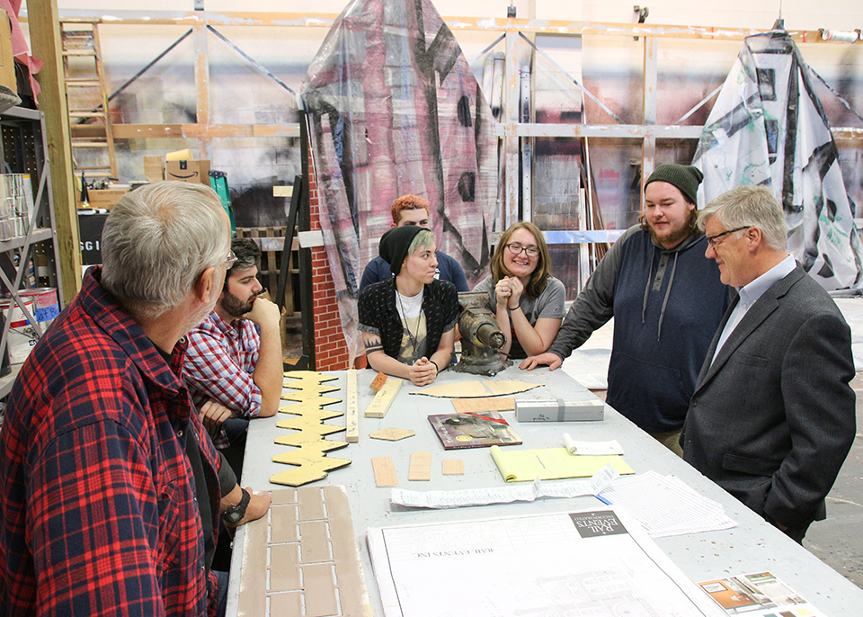 Dean Hixson and students talking around scene shop work table