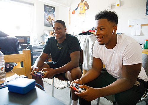 housing - two male students play video games in dorm room