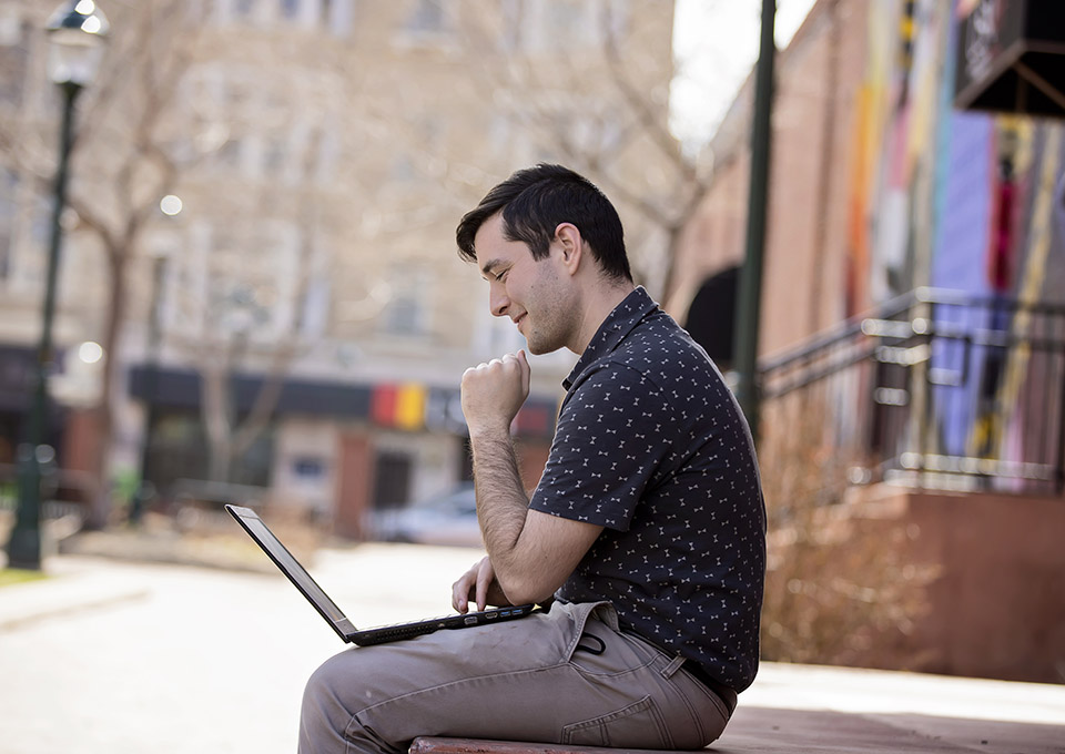 John Paul outside sitting on FSU campus wall with computer