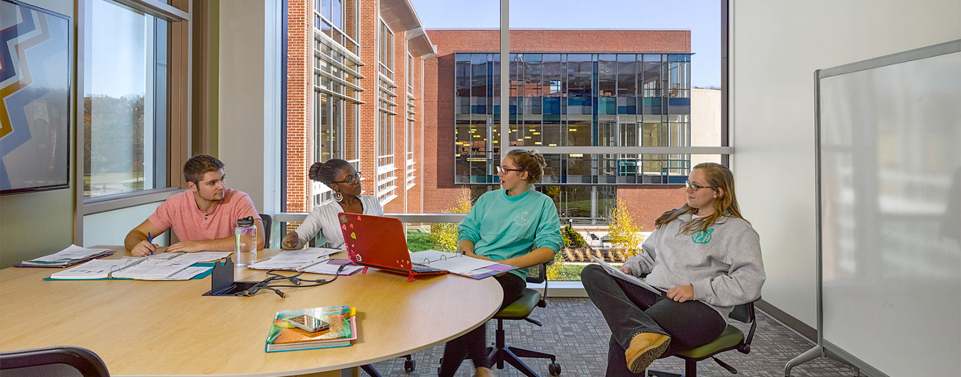 4 students sit in a study room in the Gira Center and work on a group project