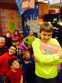 Boy happily clutching 'Hug Machine' with smiling class in background