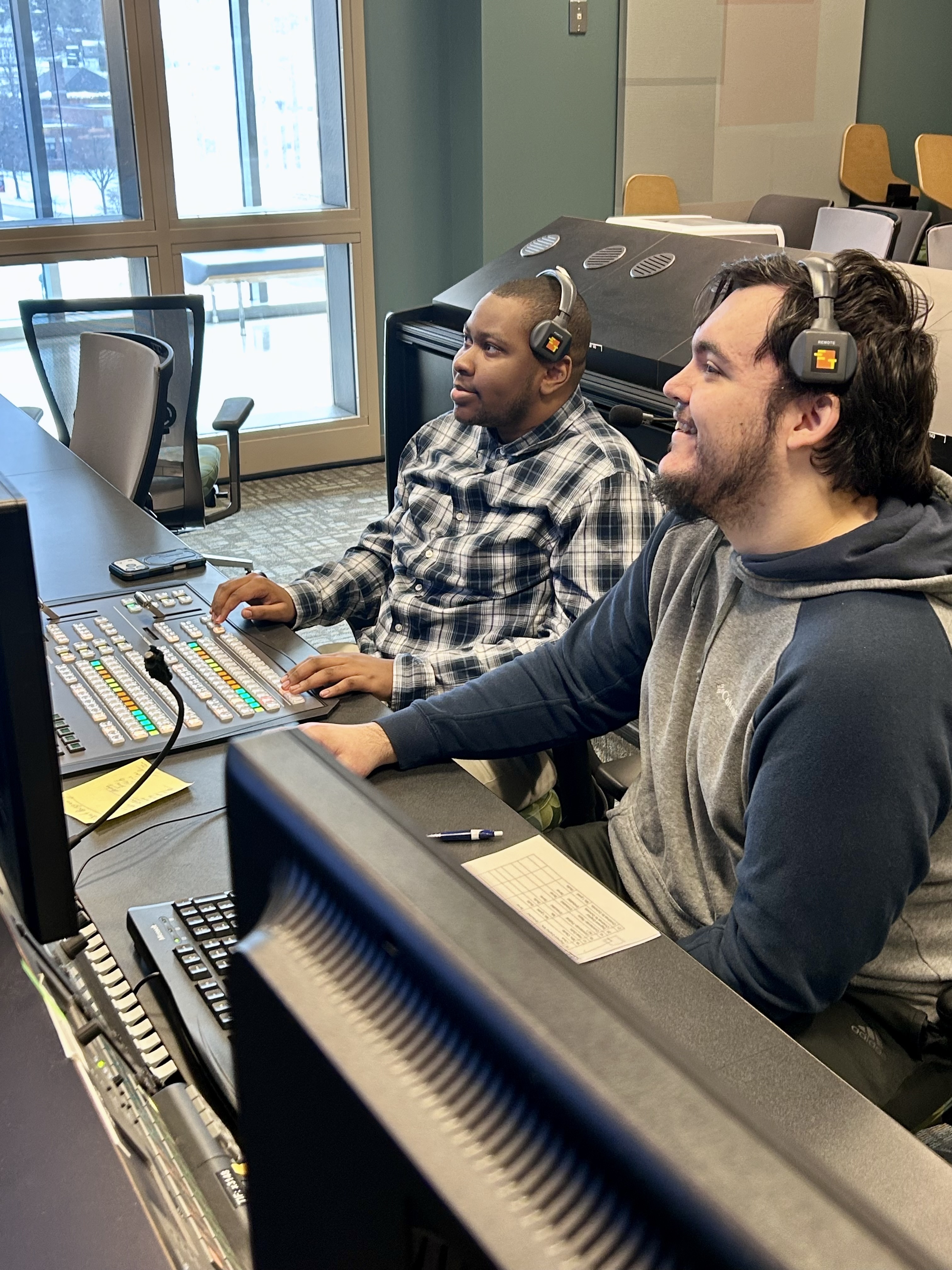Two students with headsets operate studio video control board