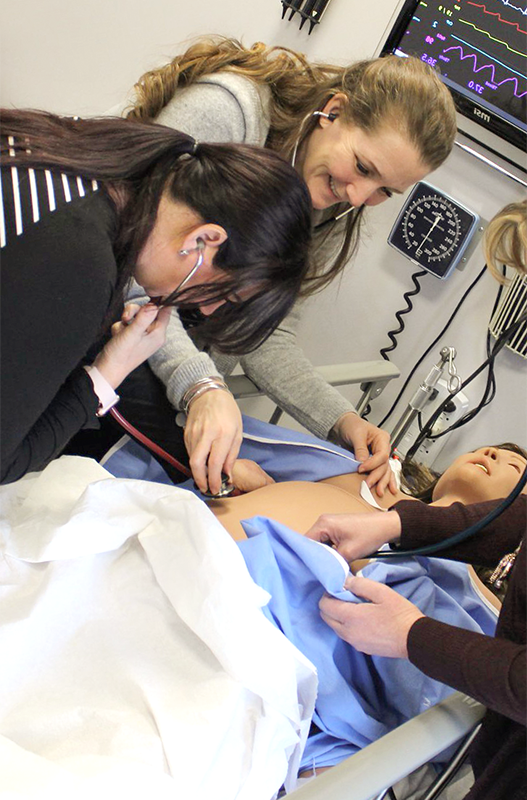 nursing student listens to a manikin's heart with professor supervising