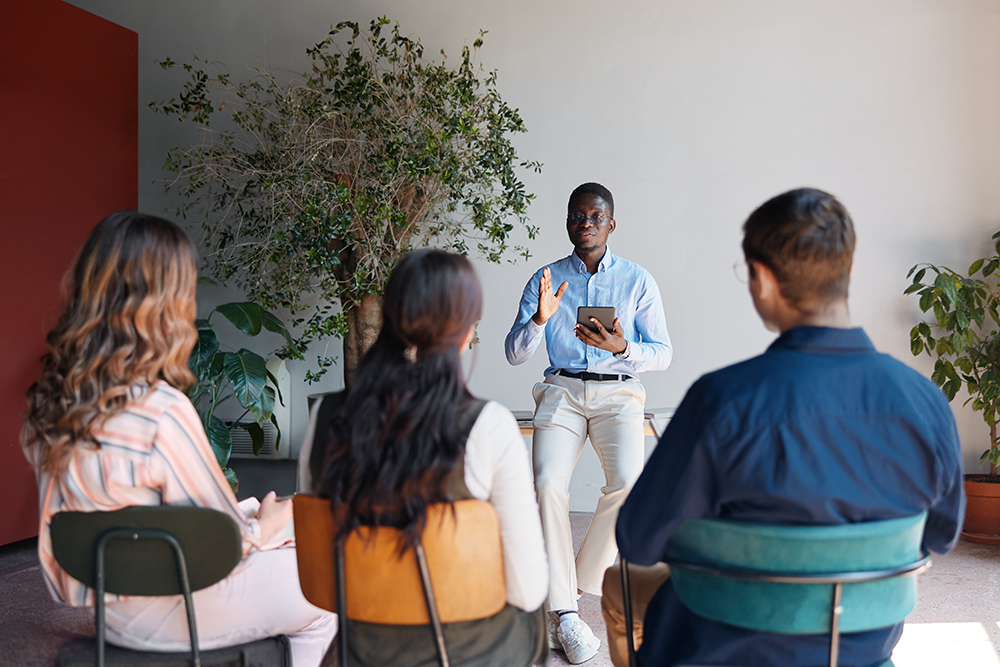 FSU Entrepreneurship HUB-An African American business coach standing at the front of a room, leading an engaging training seminar for a diverse group of professionals.