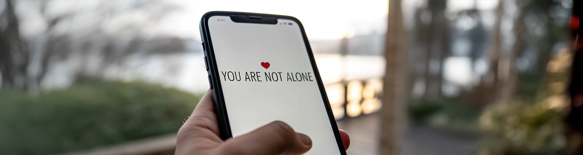holding a phone that shows a heart emoji with the message and a message "You are not alone"