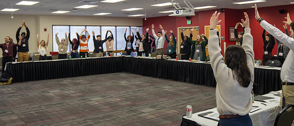 Photo of students standing around table with hands in air