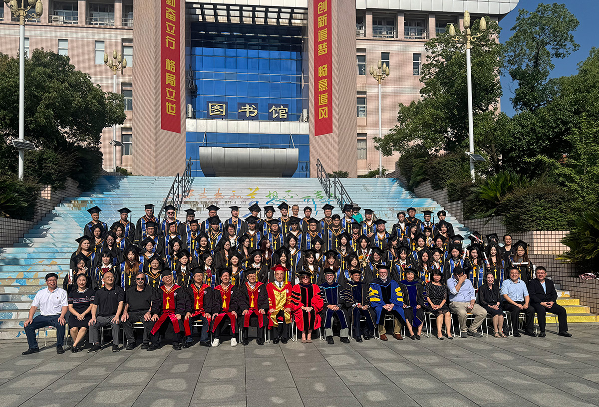 Large group of graduates and faculty in academic robes posing for a group photo on outdoor steps in front of a university building