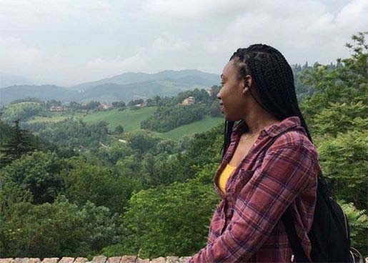 student looking out over a stone fence into the countryside